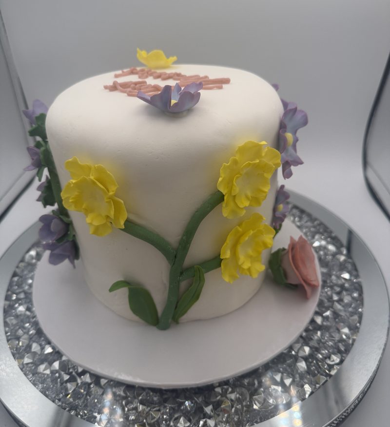 Side of the white fondant &ldquo;Just Married&rdquo; cake with yellow sugar daffodils, purple flowers and a pink rose