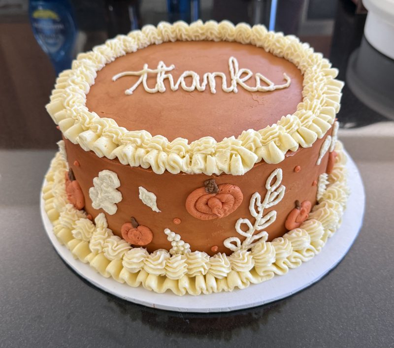 Caramel-colored cake piped with &ldquo;thanks&rdquo;, cream ruffle borders, pumpkins and leaves
